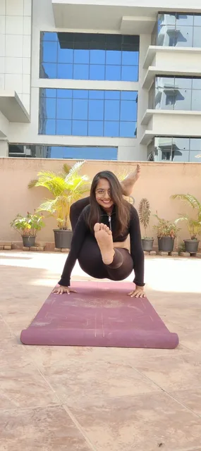 Dhruvi practising a seated yoga balance on a terrace