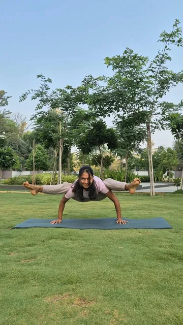 Dhruvi practising a wide-legged arm balance outdoors
